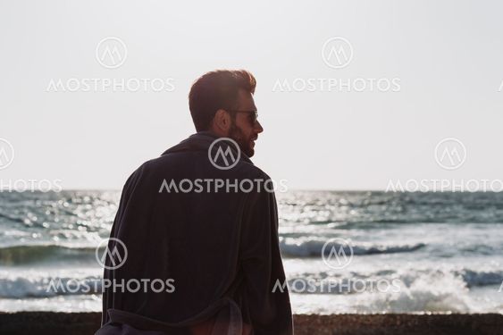 Young man in a bathrobe on the beach in sunset