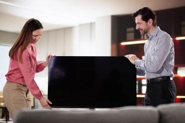 Smiling husband and wife carefully moving new television...