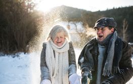 Beautiful senior couple blowing snow in sunny winter nature