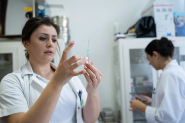 A focused nurse in a white lab coat carefully prepares a...