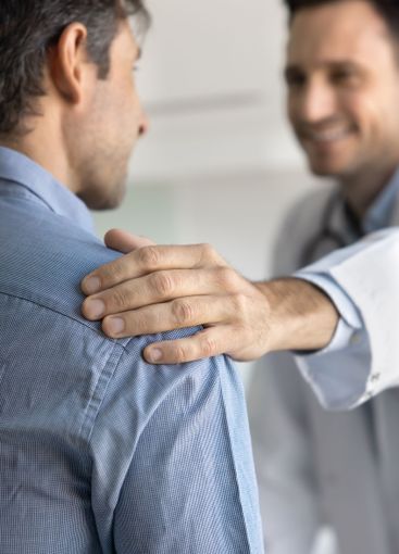 Hand of positive young male doctor touching shoulder of...