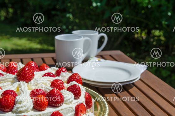Table with strawberry cake and coffee cups in background