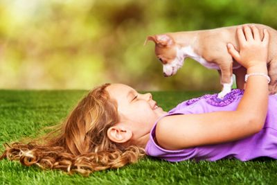 Happy Girl and Puppy Laying on Grass Outdoors