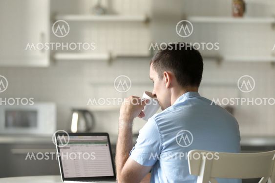 Portrait of a young man at desk with a laptop, drinking