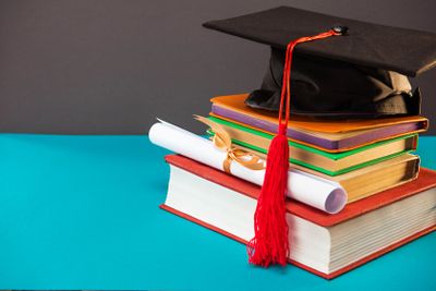 books, diploma and graduation cap with tassel on blue...