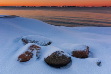 Snow-covered rocks at the shoreline during sunset on a...