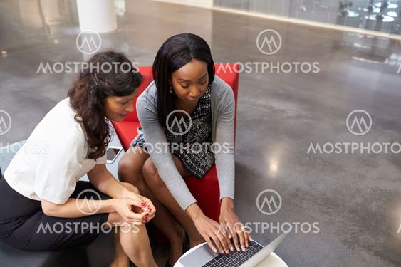 Two Businesswomen Using Laptop In Lobby Of Modern Office