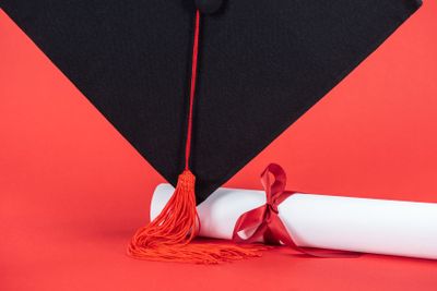 Academic cap with tassel and diploma with ribbon on red...