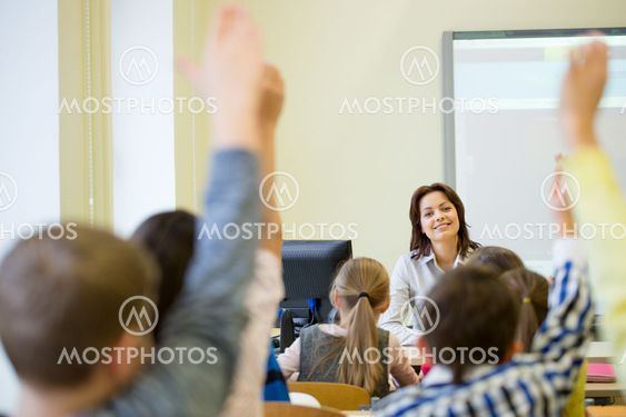 group of school kids raising hands in classroom