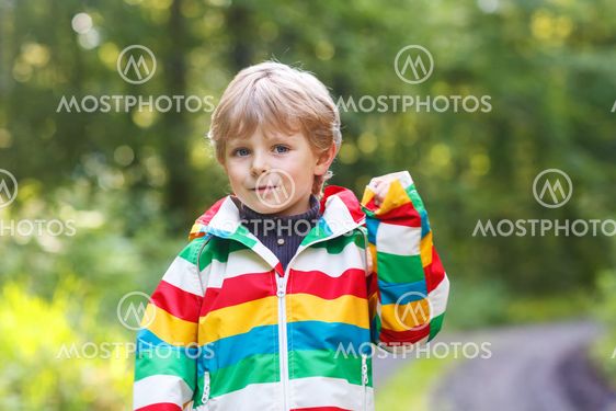 Portrait of blond little preschool boy in colorful waterproof raincoat in autumn forest