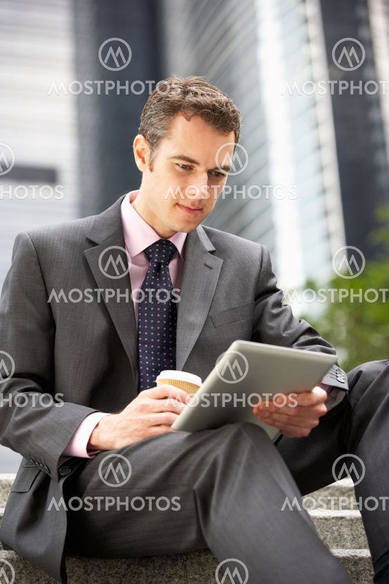 Businessman Working On Tablet Computer Outside Office With Takeaway Coffee