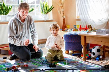Father and son playing with racing cars on racetrack,...