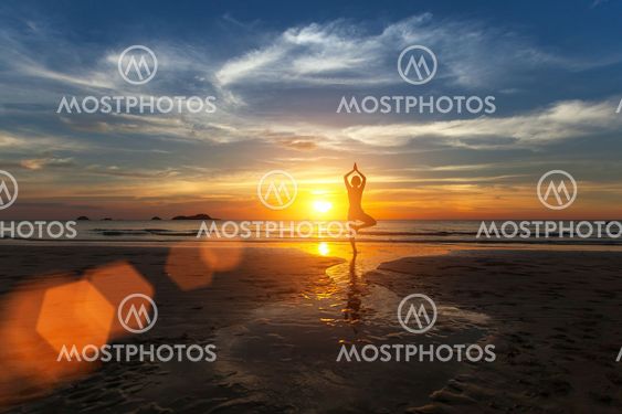 Small silhouette of a woman practicing yoga on sea beach during amazing sunset.