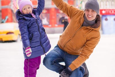 Little happy girl with young father have fun on skating rink