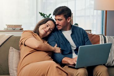 Pregnancy, laptop and couple relax in home together to...