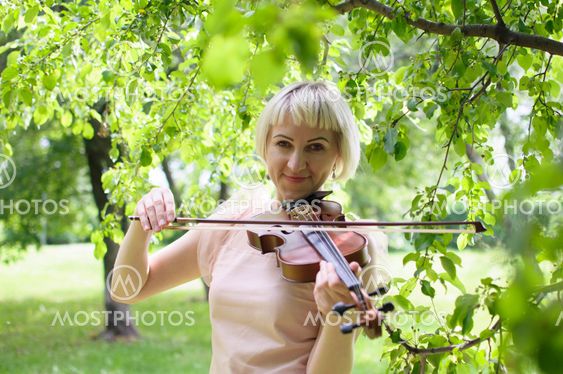 The Russian woman plays a violin in the park in the summer.