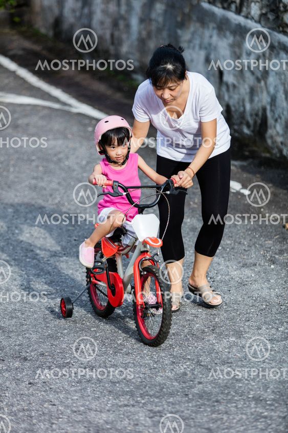 Asian Chinese little girl riding bicycle with mom guide