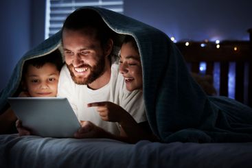 Happy, parents and child relax on tablet at night of...