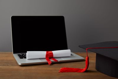 Laptop with blank screen, diploma and academic cap with...
