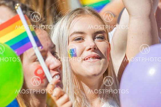 Young blond woman with the rainbow flag painted on cheek...
