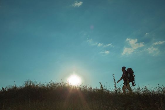Young caucasian man with backpack walking on a green meadow