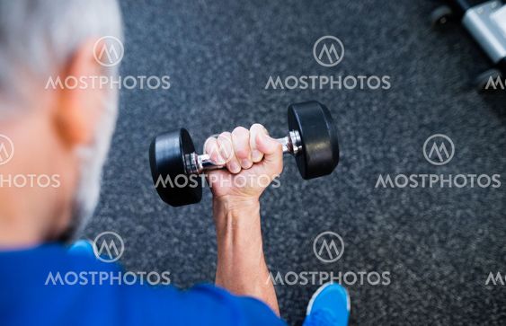 Unrecognizable senior man in gym working out with weights.