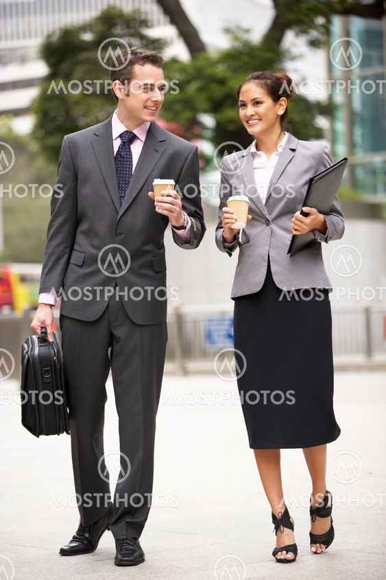 Businessman And Businesswoman Walking Along Street Holding Takeaway Coffee