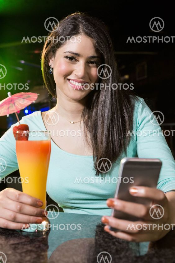Beautiful woman typing a text message while having cocktail
