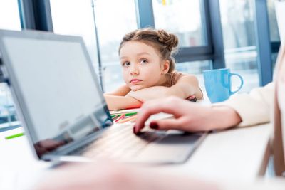 businesswoman working with laptop while daughter looking...