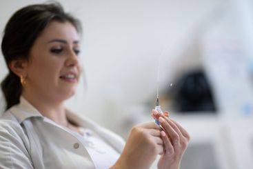 A focused nurse in a white lab coat carefully prepares a...