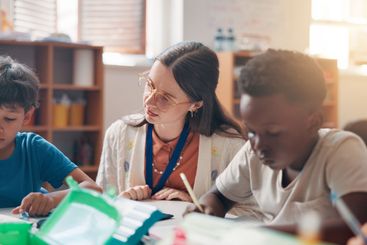 Writing, education and teacher helping kids in classroom...