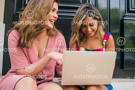 Two friends using laptop outdoors.