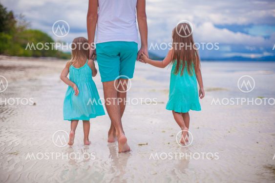 Back view of young father and his two little kids walking by the sea