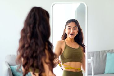 Portrait of slim Indian woman measuring her waist in...