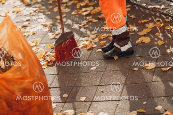 Janitor cleaner sweeping autumn leaves on the street