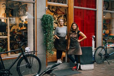 Smiling female coworkers standing at doorway of bicycle...