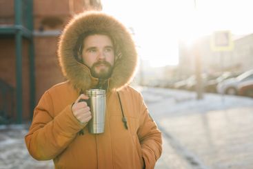 Man enjoying warm drink in sunlight on cold winter urban...