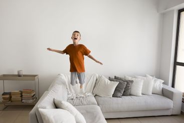 Cute little 6s boy having fun, jumping on cozy sofa