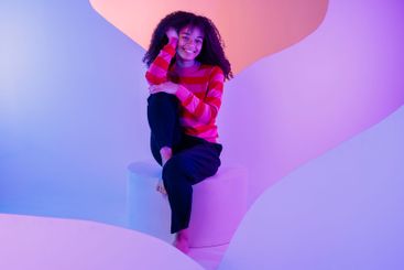 African in sweater sits at white round platform....