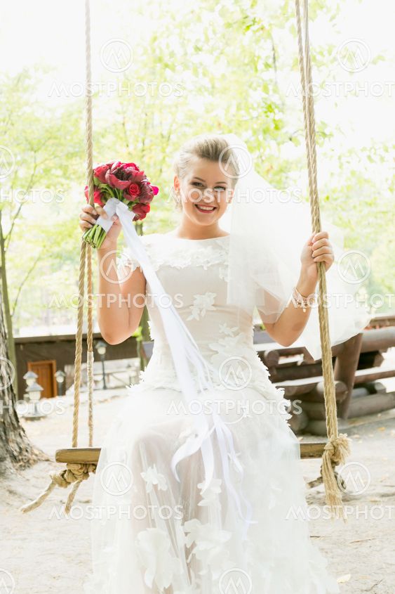 Toned portrait of beautiful bride swinging on swing at park