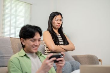 A moody girl sits in the living room, feeling ignored by...