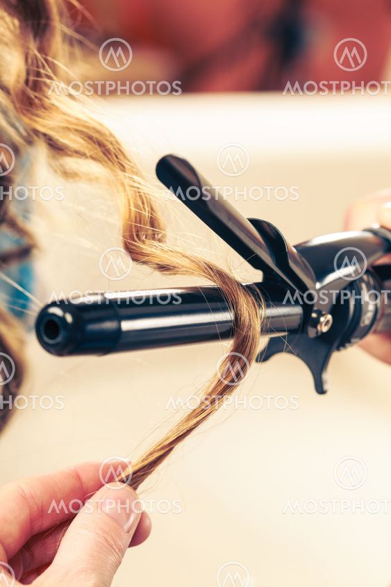 Stylist curling hair for young woman.