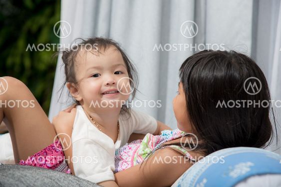 Cute Asian girl playing with her sister on bed at home.