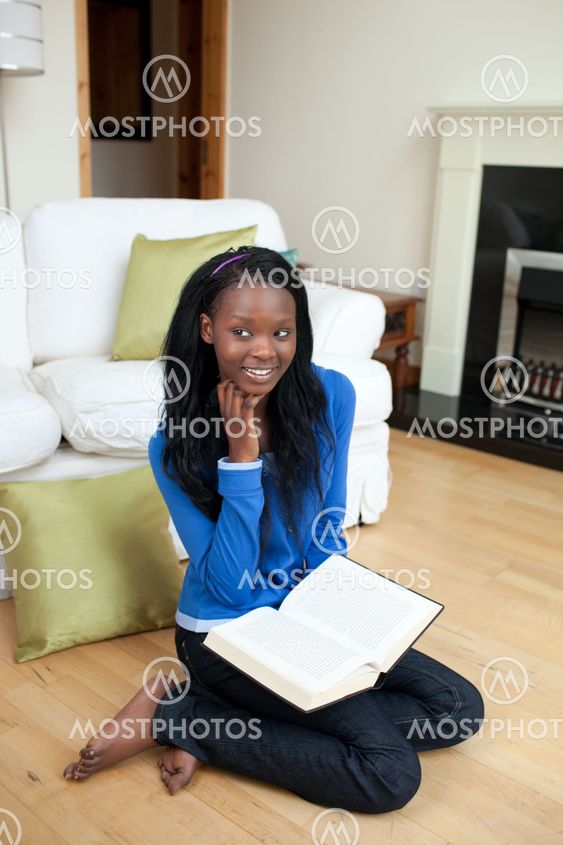 Smiling woman reading a book sitting on the floor
