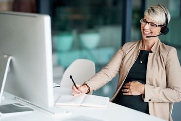 Computer, headset and businesswoman writing notes in...