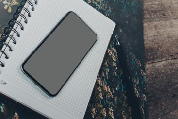 Smartphone resting on a blank notepad on a textured...