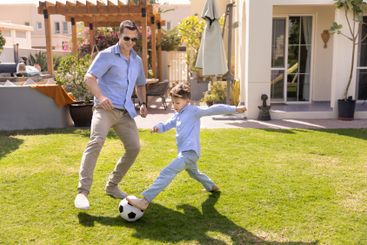Positive father and active soccer player son boy kicking...