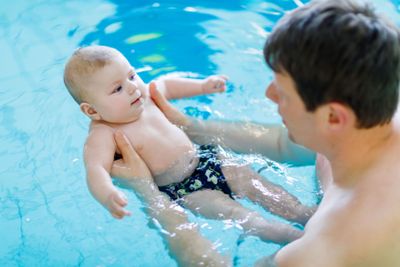 Happy middle-aged father swimming with cute adorable baby...