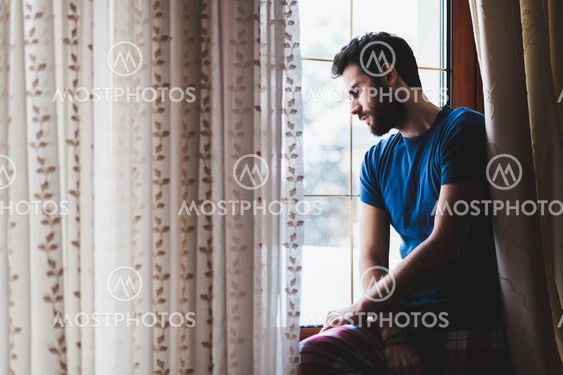 Young sad mad sitting by the window in regret