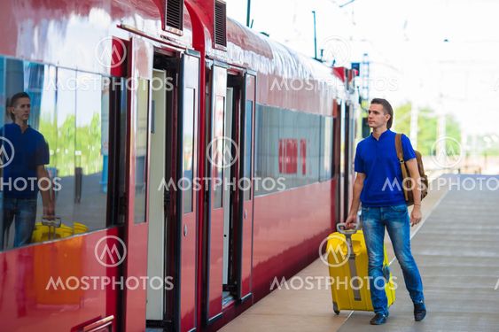 Young caucasian man with luggage at station traveling by...